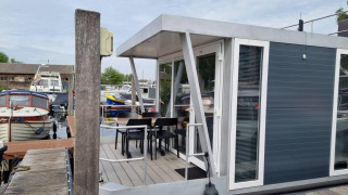 Casa flotante moderna 'De Hoop' en Marina Parcs - Jachthaven De Hoop, Países Bajos, con terraza y sillas.