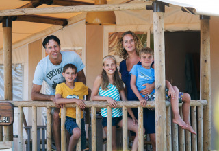 Famiglia felice sulla veranda di SunLodge Jungle al Camping Union Lido Mare in Italia, sorridenti in vacanza.