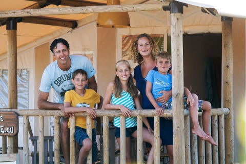 Una familia sonriente en la terraza de SunLodge Jungle en Camping Union Lido Mare, Italia, disfrutando sus vacaciones.