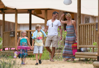 Una familia de cuatro personas pasea frente a SunLodge Jungle en Camping Union Lido Mare en Italia.
