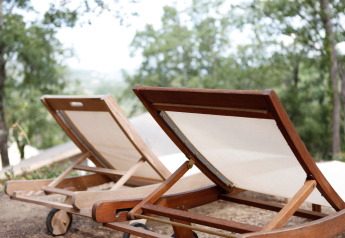 Two wooden sun loungers with white fabric backs sitting outdoors in lush greenery at SunLodge Jungle, Italy.