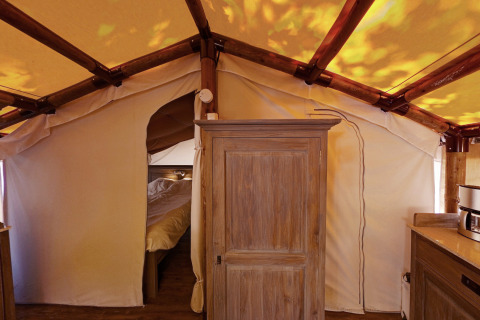Intérieur de la SunLodge Jungle avec armoire en bois, lit à l'arrière-plan et structure de tente en toile.