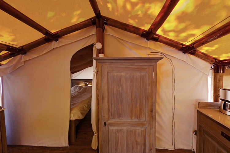Interior de SunLodge Jungle con armario de madera, cama al fondo y estructura de tienda de campaña.