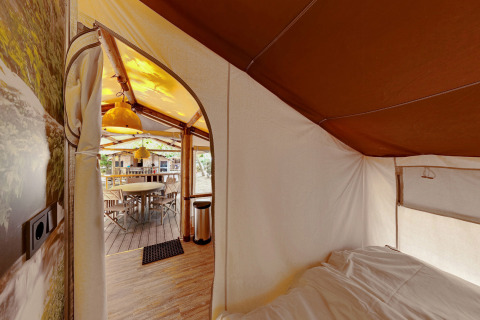 Binnen in SunLodge Jungle, zicht vanuit bed op de eettafel met houten stoelen onder tentdoek.