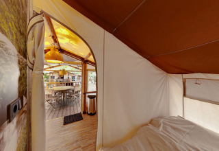 Vista interior de SunLodge Jungle desde la cama hacia el comedor al aire libre con muebles de madera.