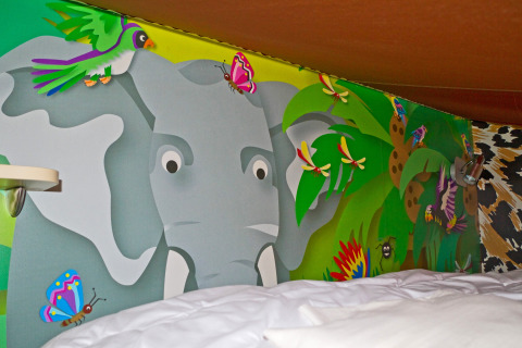 Kleurrijk junglewandtekening met olifant, vlinders en vogels boven bed in SunLodge Jungle, Union Lido, Italië.