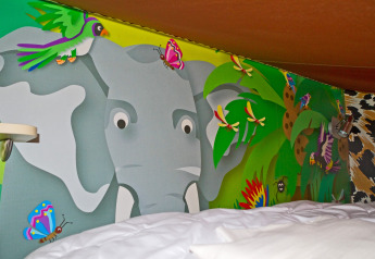 Murale colorato a tema giungla con elefante, farfalle e uccelli sopra il letto al SunLodge Jungle, Union Lido, Italia.