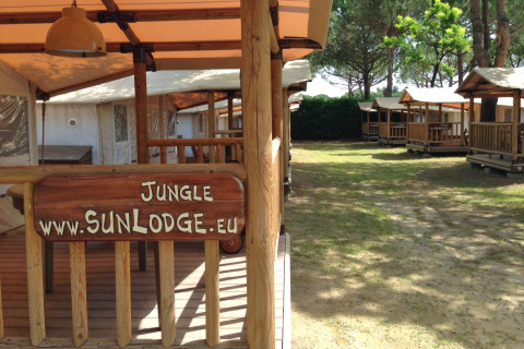 Bungalow SunLodge Jungle al Camping Union Lido Mare in Italia, insegne in legno e pini visibili.