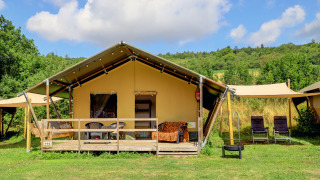 Safari tent lodge set amidst greenery, featuring a wooden deck, outdoor chairs, and relaxing views.