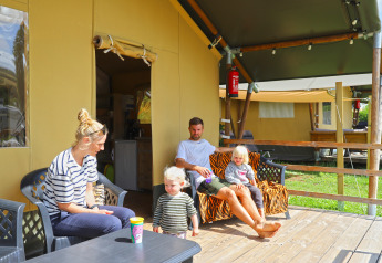 Familie slapper af foran et safaritelt på Camping Walsheim, Tyskland, omgivet af campingudstyr.