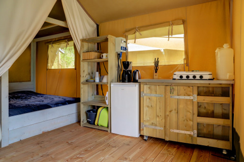 Interior de tienda safari con cama, cocina pequeña y estantes de madera en Camping Walsheim, Alemania.