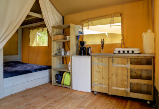 Interno tenda safari con letto, piccola cucina e scaffali in legno al Camping Walsheim in Germania.