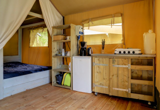 Indretning af Safari-telt med seng, lille køkken, træhylder og vinduer på Camping Walsheim i Tyskland.