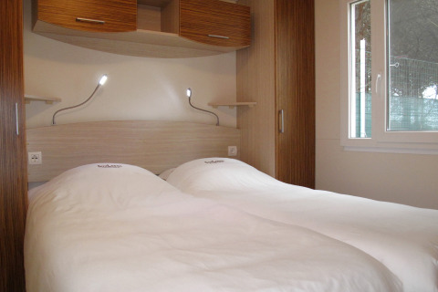 Dos camas individuales con sábanas blancas y lámparas de lectura en una moderna habitación de glamping.