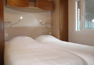 Dos camas individuales con sábanas blancas y lámparas de lectura en una moderna habitación de glamping.