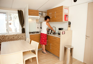 Femme faisant la vaisselle dans une kitchenette moderne au glamping SunLodge Redwood avec coin repas.