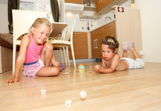 Dos niños juegan con dados en el suelo de una acogedora cabaña con cocina moderna de fondo.