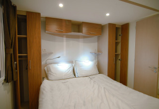 Dormitorio en una cabaña con cama doble, armarios empotrados y muebles de madera bajo luces cálidas.