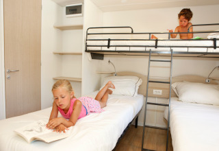 Dos niños leen en camas separadas en una habitación luminosa y moderna de un lodge con litera y decoración sencilla.