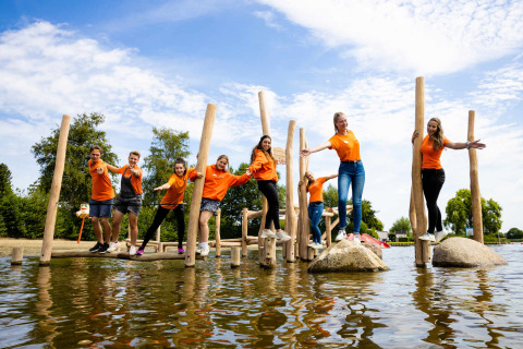 Grupo de jóvenes con camisetas naranjas disfruta de parque acuático en un camping glamping soleado.