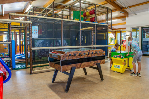 Zona de juegos interior en un parque vacacional con niños, futbolín y área de escalada moderna.
