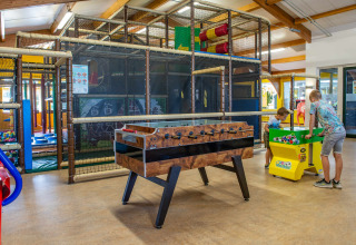 Zona de juegos interior en un parque vacacional con niños, futbolín y área de escalada moderna.