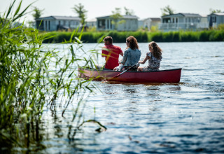 Gezin vaart met kano op meer bij vakantiepark met glamping en moderne chalets op de achtergrond.