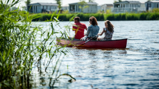 Familia remando en canoa en un lago en un parque vacacional con glamping y casas al fondo.
