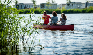Familia remando en canoa en un lago en un parque vacacional con glamping y casas al fondo.
