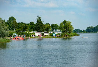 Ferienpark am See mit Glamping-Unterkünften, Gästen beim Baden, Spielen und Entspannen am Ufer.