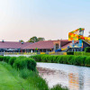Photo of a holiday park with glamping, colorful waterslide, scenic canal, and lush green surroundings.