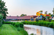 Foto af feriepark med glamping, farverig vandrutsjebane, kanal og grønne omgivelser ved solnedgang.