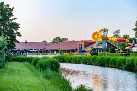 Foto van een vakantiedomein met glamping, kleurrijke waterglijbaan, kanaal en groene omgeving.