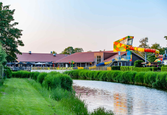 Foto eines Ferienparks mit Glamping-Unterkünften, bunter Wasserrutsche, Fluss und viel Grün.
