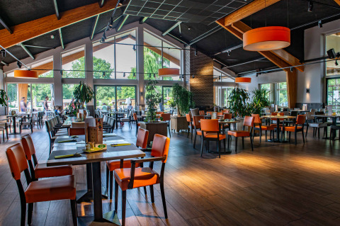 Interior luminoso y moderno de restaurante con grandes ventanales y sillas naranjas en un parque de glamping.