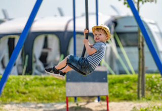 Niño con camiseta de rayas y sombrero juega en un columpio en parque de vacaciones con glamping.