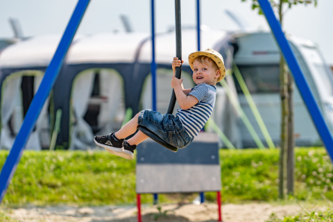 Garçon en t-shirt rayé sur une balançoire dans un parc de vacances avec hébergements glamping.