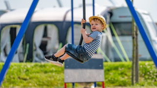 Niño con camiseta de rayas y sombrero juega en un columpio en parque de vacaciones con glamping.