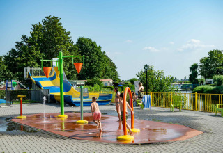 Kinderen spelen op een waterspeelplein in een vakantiepark met glamping, glijbanen en veel groen.