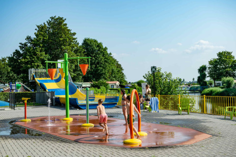 Kinderen spelen op een waterspeelplein in een vakantiepark met glamping, glijbanen en veel groen.