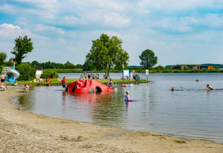 Gezinnen genieten van het water en het strand in een vakantiepark met glamping aan een recreatiemeer.