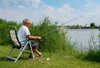 Uomo anziano pesca seduto vicino al lago in una sedia, in un parco vacanze con alloggi glamping.