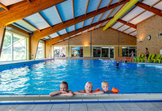 Indendørs swimmingpool med tre glade børn ved kanten, feriepark tilbyder glamping og sjove aktiviteter.