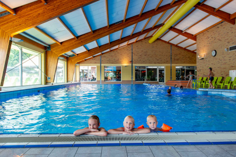 Piscine intérieure dans un parc de vacances, trois enfants au bord, séjour glamping confortable garanti.
