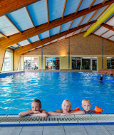 Piscina cubierta en parque vacacional, tres niños disfrutan en el borde, excelente opción de glamping.