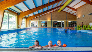 Piscina cubierta en parque vacacional, tres niños disfrutan en el borde, excelente opción de glamping.