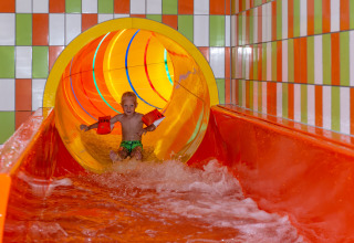 Kind met zwembandjes op een kleurrijke waterglijbaan in een vakantiepark met glamping accommodaties.
