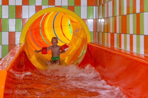 Kind met zwembandjes op een kleurrijke waterglijbaan in een vakantiepark met glamping accommodaties.