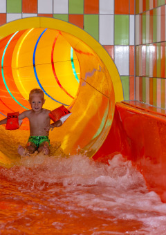 Niño con manguitos baja por un tobogán acuático colorido en un parque de vacaciones con glamping.