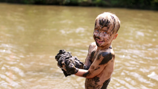 Smiling child covered in mud playing by a river at a holiday park offering glamping accommodations.